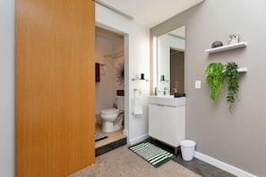 Casa de banho moderna com sanita, lavatório, espelho e plantas verdes em prateleiras.