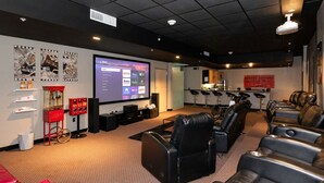 A home theater room with a large screen, multiple seating areas, and a kitchen in the background. - 2 units in 1! Silver Screen Getaway - Downtown Dsm (Des Moines)