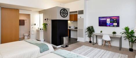 Ett hotellrum med två sängar, ett skrivbord, en TV och ett litet kök.
