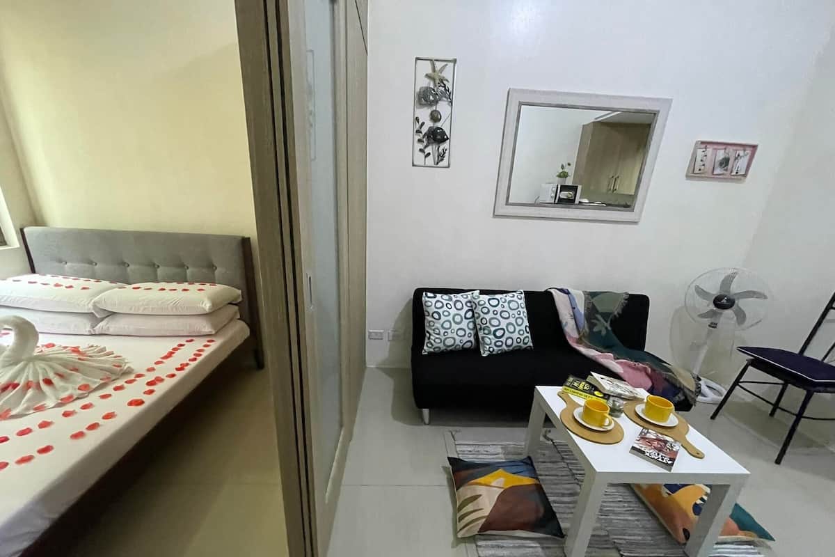 Un dormitorio con una cama, un sofá, una mesita con objetos, un espejo y un ventilador.