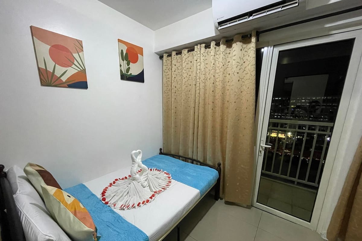Un dormitorio pequeño con una cama individual, una ventana con cortinas y dos cuadros colgados en la pared.
