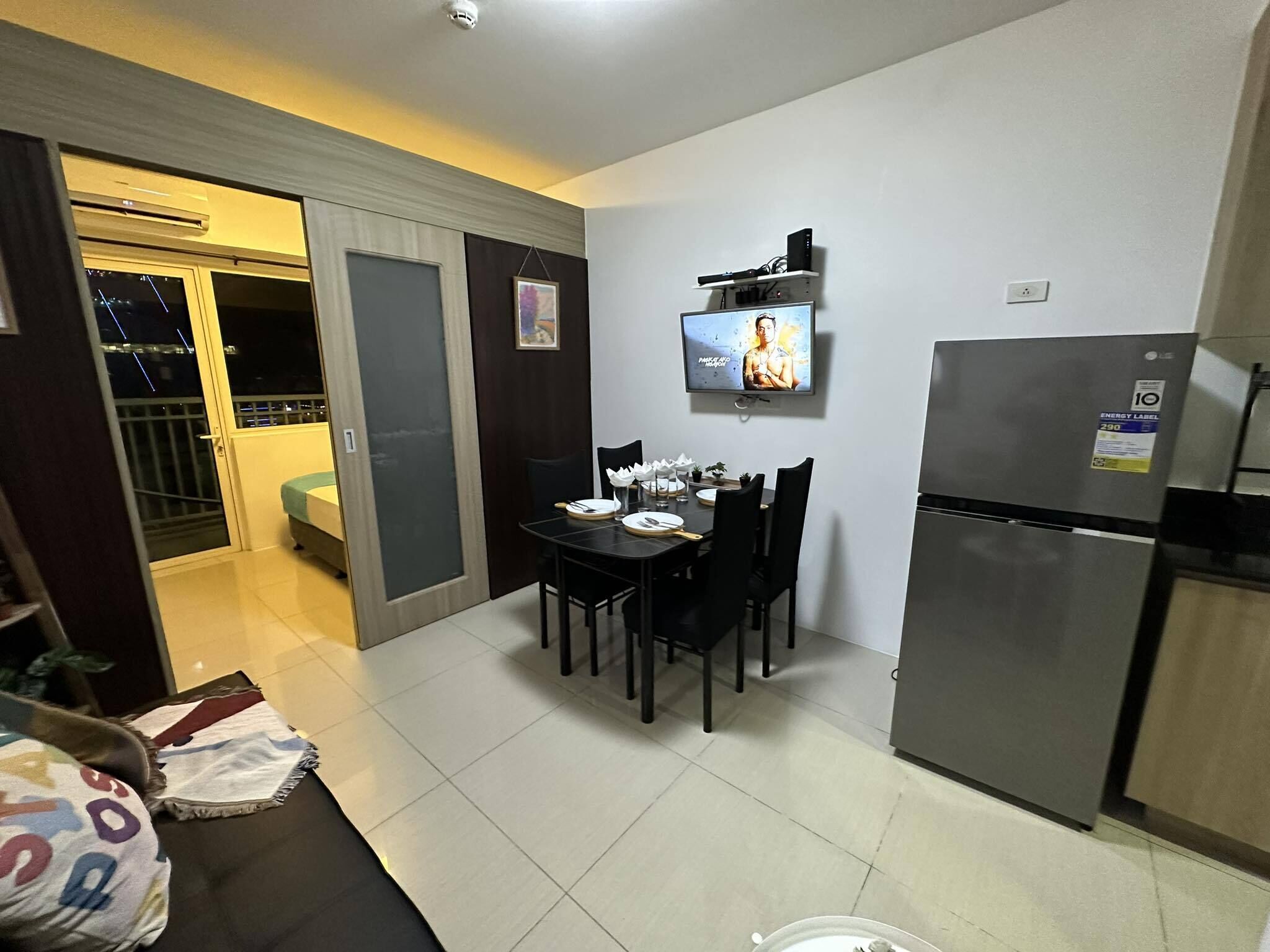 Una cocina compacta con una mesa de comedor para dos personas, un refrigerador y un televisor montado en la pared.
