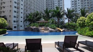 A resort pool with lounge chairs, surrounded by palm trees and a waterfall feature.