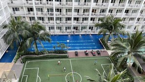 A hotel with a rooftop pool, a tennis court, and palm trees.