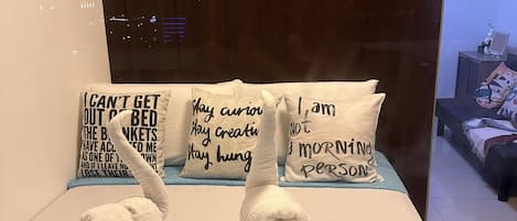 A hotel room with a bed, a blue textured rug, and three pillows with motivational quotes.