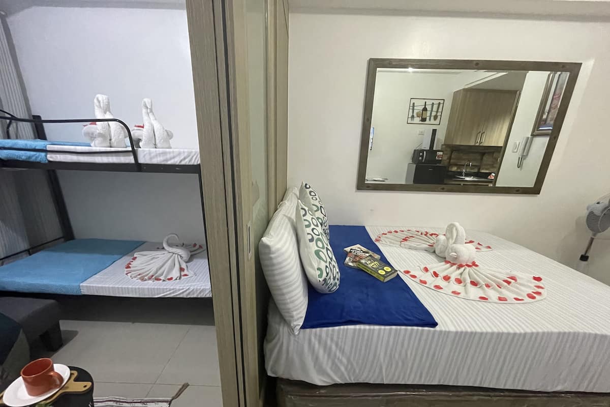Una habitación de hotel con literas, una cama individual con una manta azul, una almohada, una toalla y una mesita con una taza y un platito.