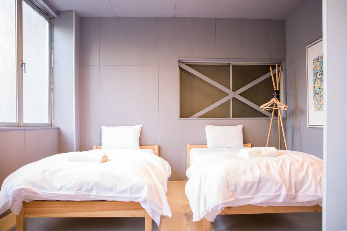 Quarto com duas camas de solteiro, uma janela, uma obra de arte na parede e piso de madeira.