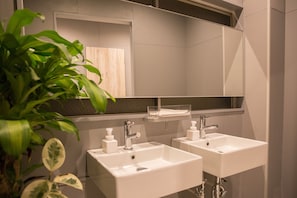 A modern bathroom with two sinks, a mirror, and a potted plant. - Hostel STAND BY ME (Fukuoka)