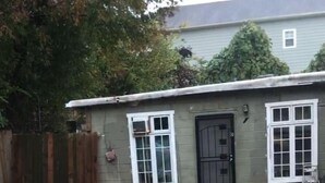 Ein Garten mit Betonplatten, einem Holzzaun und einem Haus mit schwarzem Eingang und weißen Fenstern.