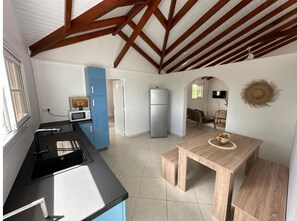 Compact kitchen area with microwave, refrigerator, and dining table, featuring a sloped ceiling with exposed beams.