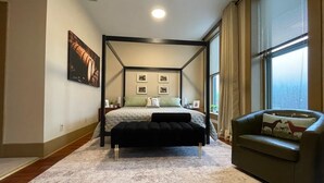 A four-poster bed with a headboard, a green armchair, and a large window with blinds. - The Top Shelf on the Bourbon Trail in Historical Downtown Versailles (Versailles)