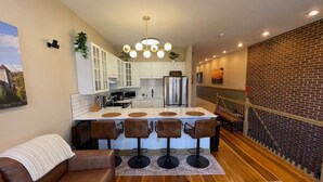 A modern kitchen with white cabinets, a central island with bar stools, a stainless steel refrigerator, and a hanging light fixture. - The Top Shelf on the Bourbon Trail in Historical Downtown Versailles (Versailles)