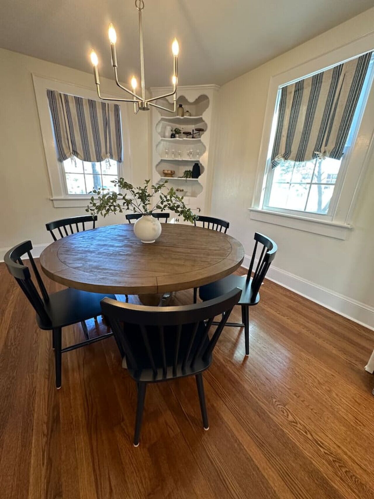 A round dining table with six chairs, a chandelier, and a vase with plants.