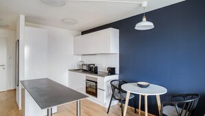 Une cuisine moderne avec des armoires blanches, un four encastré et un four à micro-ondes. On y trouve également un coin repas avec une table ronde et quatre chaises.