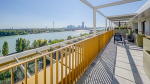 Un balcon avec vue sur la rivière, des sièges à l’extérieur et, en arrière-plan, le panorama de la ville.