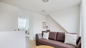 Un salon moderne avec un canapé marron, une table basse ronde en bois et une vue sur le paysage urbain, visible à travers une grande fenêtre.
