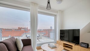 Un salon moderne avec une grande fenêtre, un canapé, une table basse, un téléviseur et un haut-parleur.