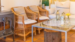 Une pièce chaleureuse avec des fauteuils en osier, une table en verre, un tronc d’arbre servant de table et un mur en pierre.