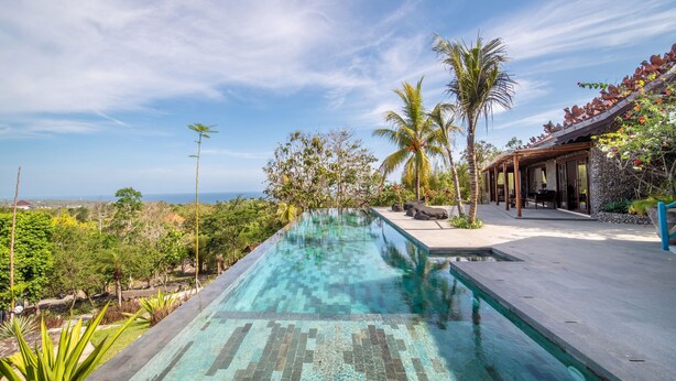 A swimming pool with a clear view of the ocean, surrounded by lush greenery and a stone building with a tiled roof. - BICKERTON ESTATE (Pecatu)