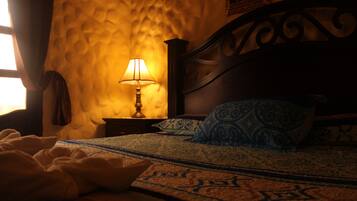 Un dormitorio con una colcha estampada, una lámpara de noche y una ventana con cortinas.