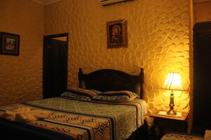 Una habitación con pared texturizada, una cama con ropa de cama estampada, una mesita de noche con lámpara y un cuadro enmarcado sobre la cama.