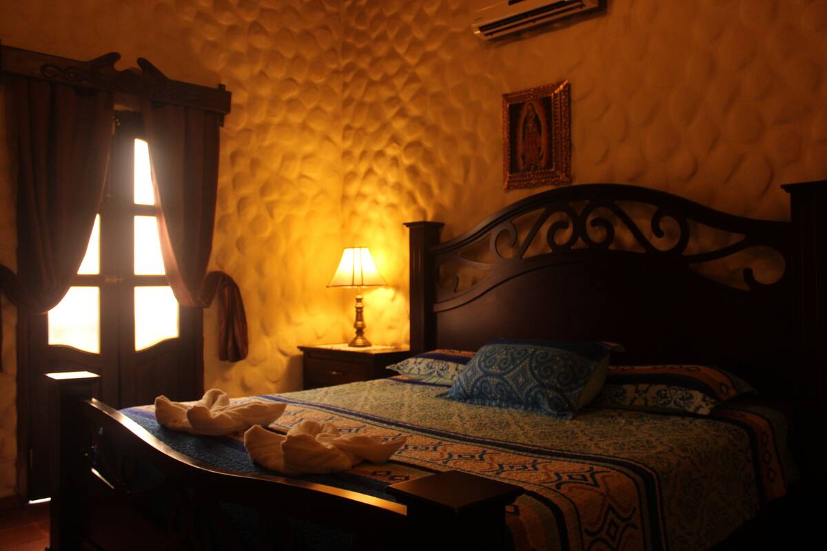 A room with a bed, a nightstand, a lamp, and a window with curtains.