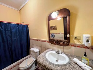 A bathroom with a white sink, a mirror, a toilet, and a shower curtain. - Hotel Caxa Real (Comayagua)