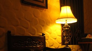 Une chaise dotée d’un dossier décoratif et une table avec une lampe, dans une pièce aux murs texturés et à l’éclairage chaleureux.