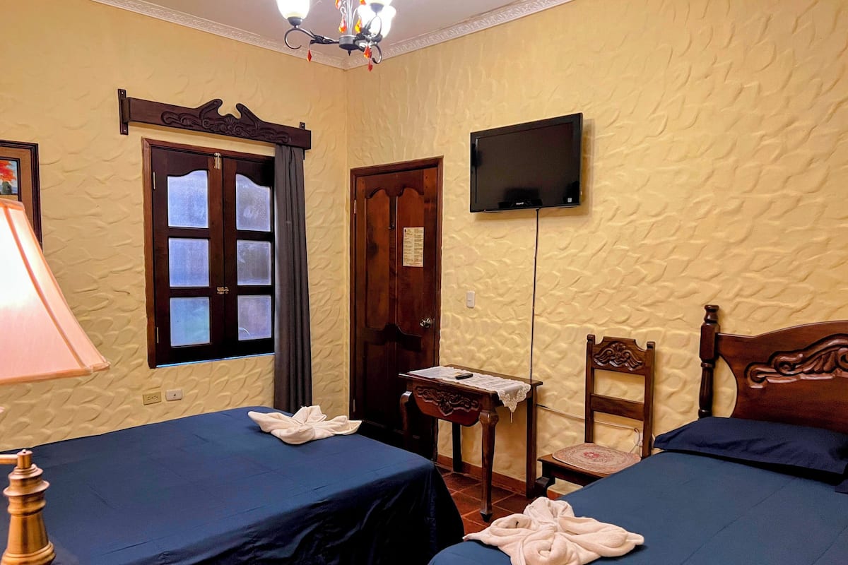 A room with two beds, a television, a lamp, and a wooden chair.