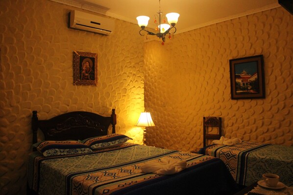 A room with a textured wall, a wooden bed with patterned bedding, a bedside lamp, and a framed picture on the wall. - Hotel Caxa Real (Comayagua)