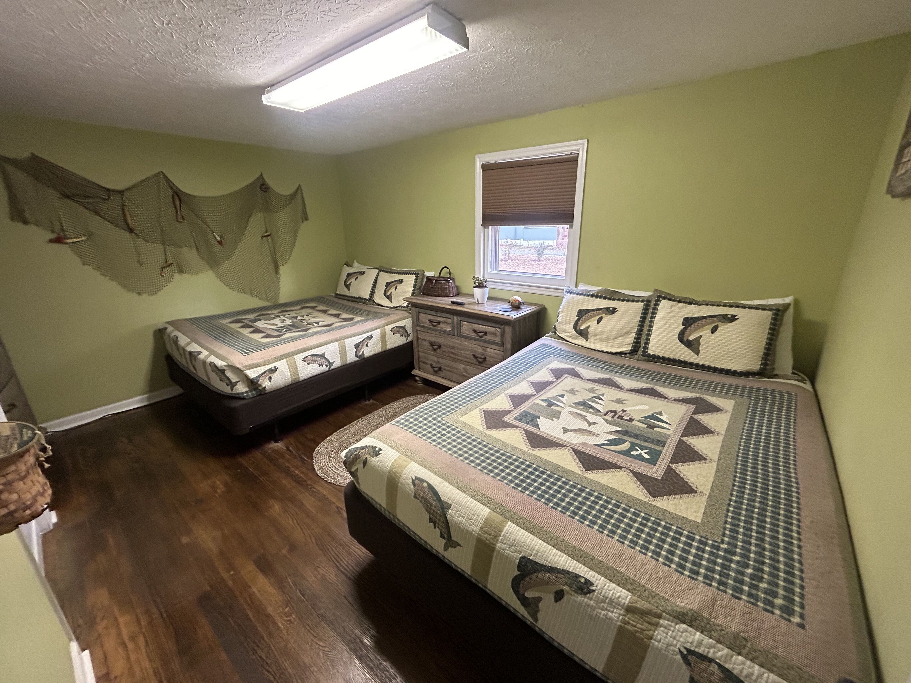 A bedroom with two beds, a dresser, a window with blinds, and a ceiling light.