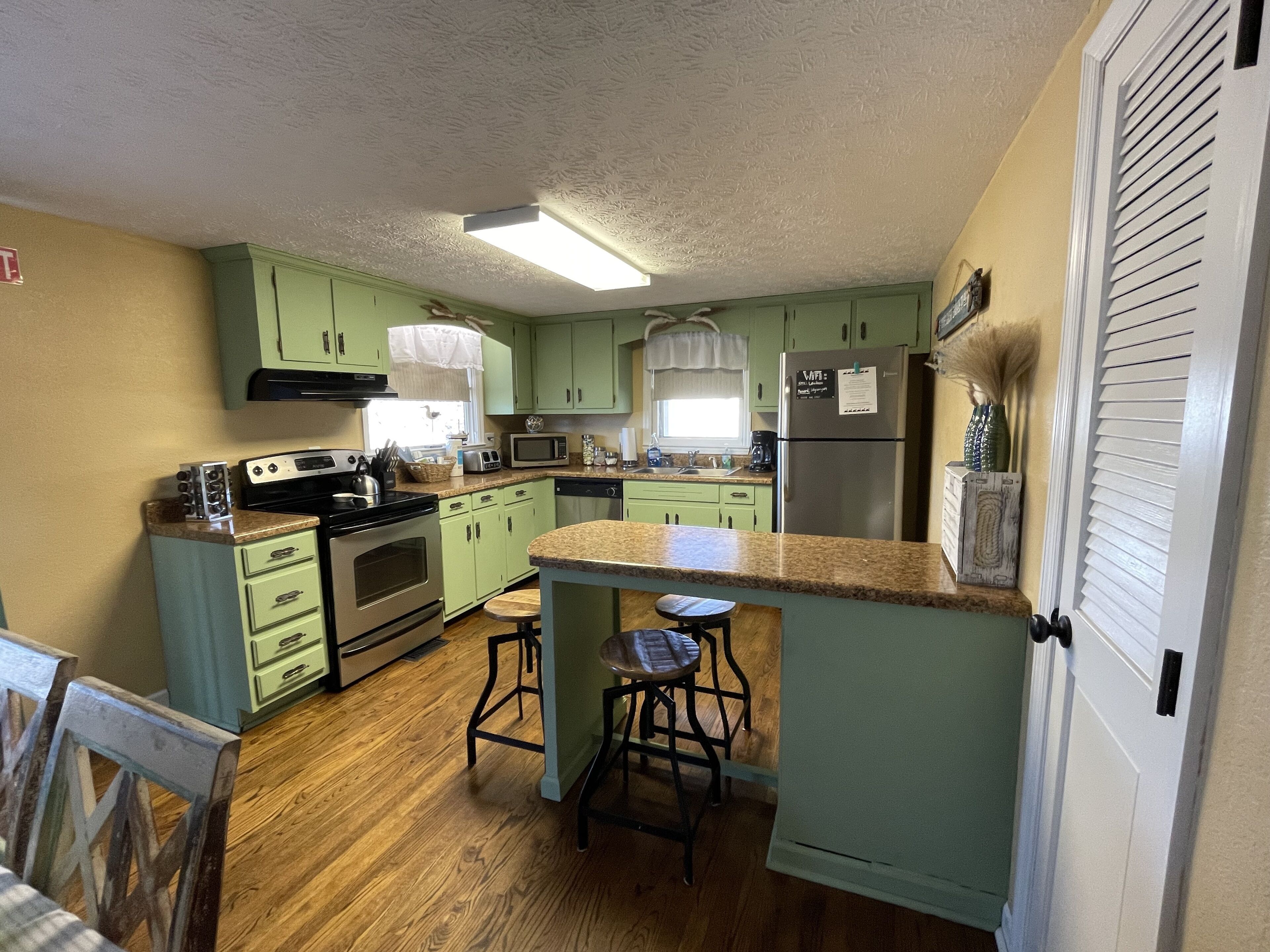 A kitchen with green cabinets, a microwave, a refrigerator, and a wooden countertop.