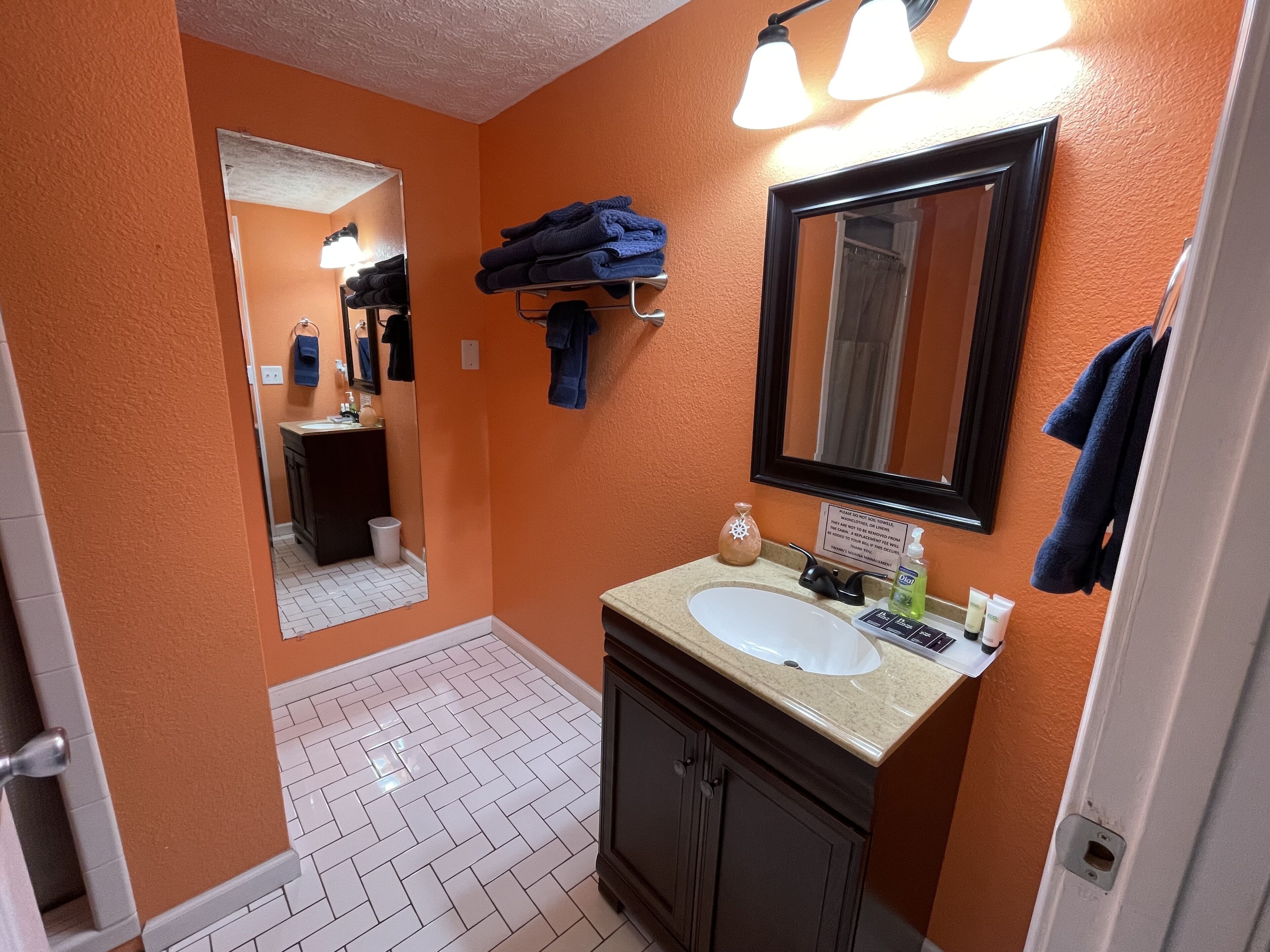 Un baño con pared naranja, un lavamanos blanco, un espejo y un perchero para toallas.