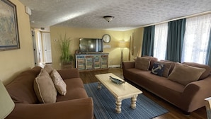 A living room with a brown sofa, a coffee table, and a television. - Beautiful Lake Front Home overlooking Lake Douglas with Hot Tub and Golf Cart! (Dandridge)