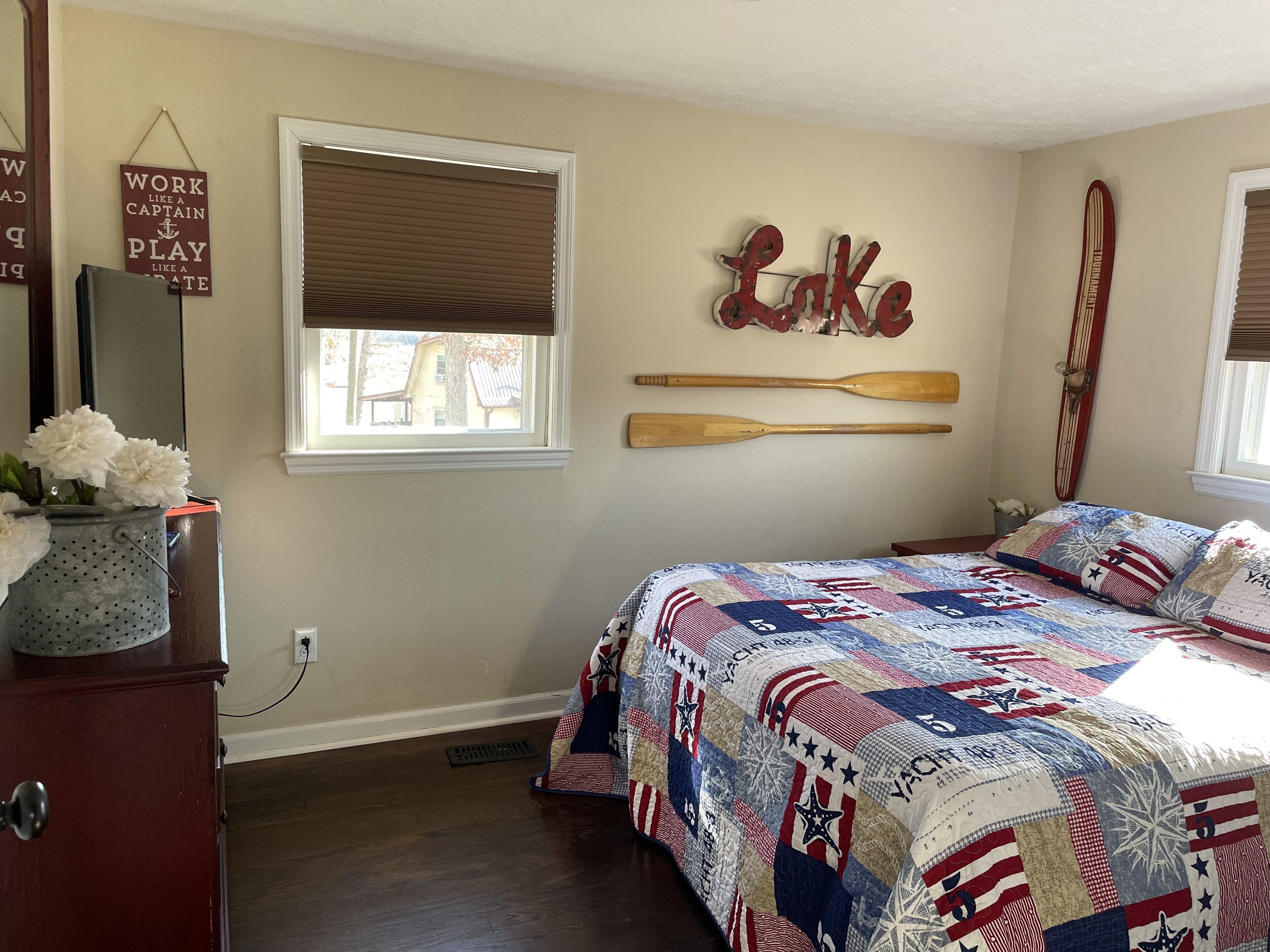 A bedroom with a bed, a window with blinds, a wall-mounted wooden paddle, and a motivational sign.