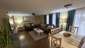 A living room with a sofa, coffee table, and chairs, a ceiling fan, and a window with curtains. - Beautiful Lake Front Home overlooking Lake Douglas with Hot Tub and Golf Cart! (Dandridge)