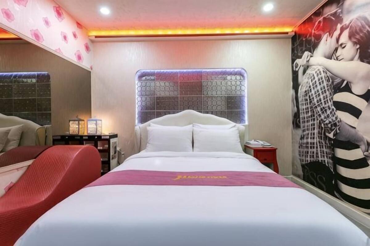 Une chambre d’hôtel avec un grand lit, un fauteuil rouge, une table de chevet et un mur orné d’une affiche.