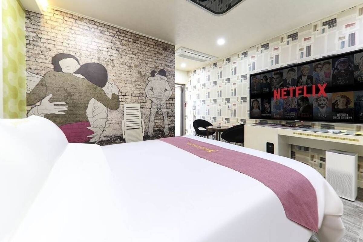Une chambre d’hôtel avec un grand lit, un bureau et un téléviseur fixé au mur, diffusant du contenu Netflix.