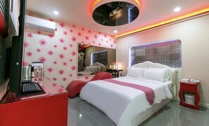 Una habitación de hotel con una cama, un escritorio con una computadora portátil, un espejo, un tocador y una ventana con cortina estampada.