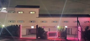 Een motel met een bord, een hek en een parkeerplaats, 's nachts.