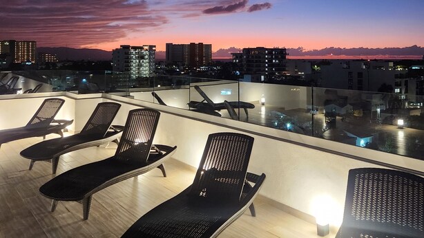 Eine Dachterrasse mit Liegestühlen und Blick auf die Skyline der Stadt in der Abenddämmerung.