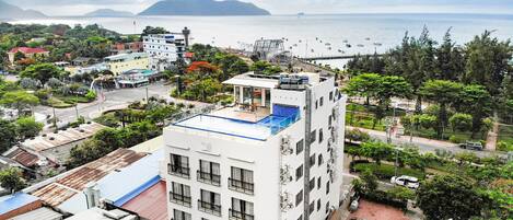 Un edificio de varios pisos con balcones, piscina en la azotea y vista al mar.
