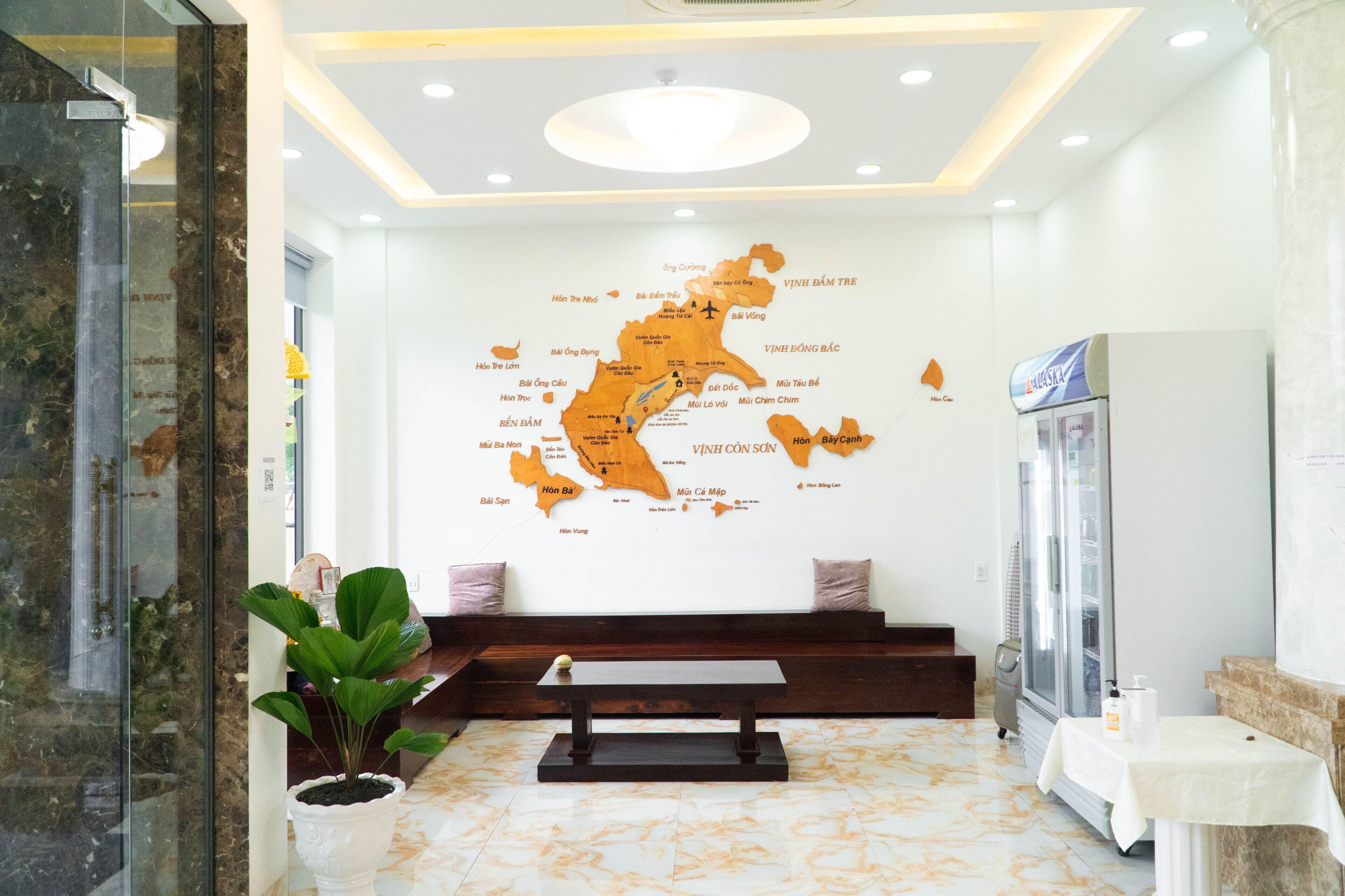 A hotel lobby with a map of Vietnam on the wall, a seating area, a reception desk, and a refrigerator.