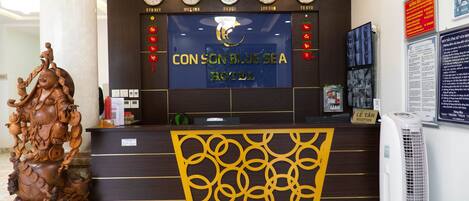 Una mesa de recepción de hotel con relojes, un cartel grande para Con Son Blue Sea Hotel y una escultura de madera decorativa.