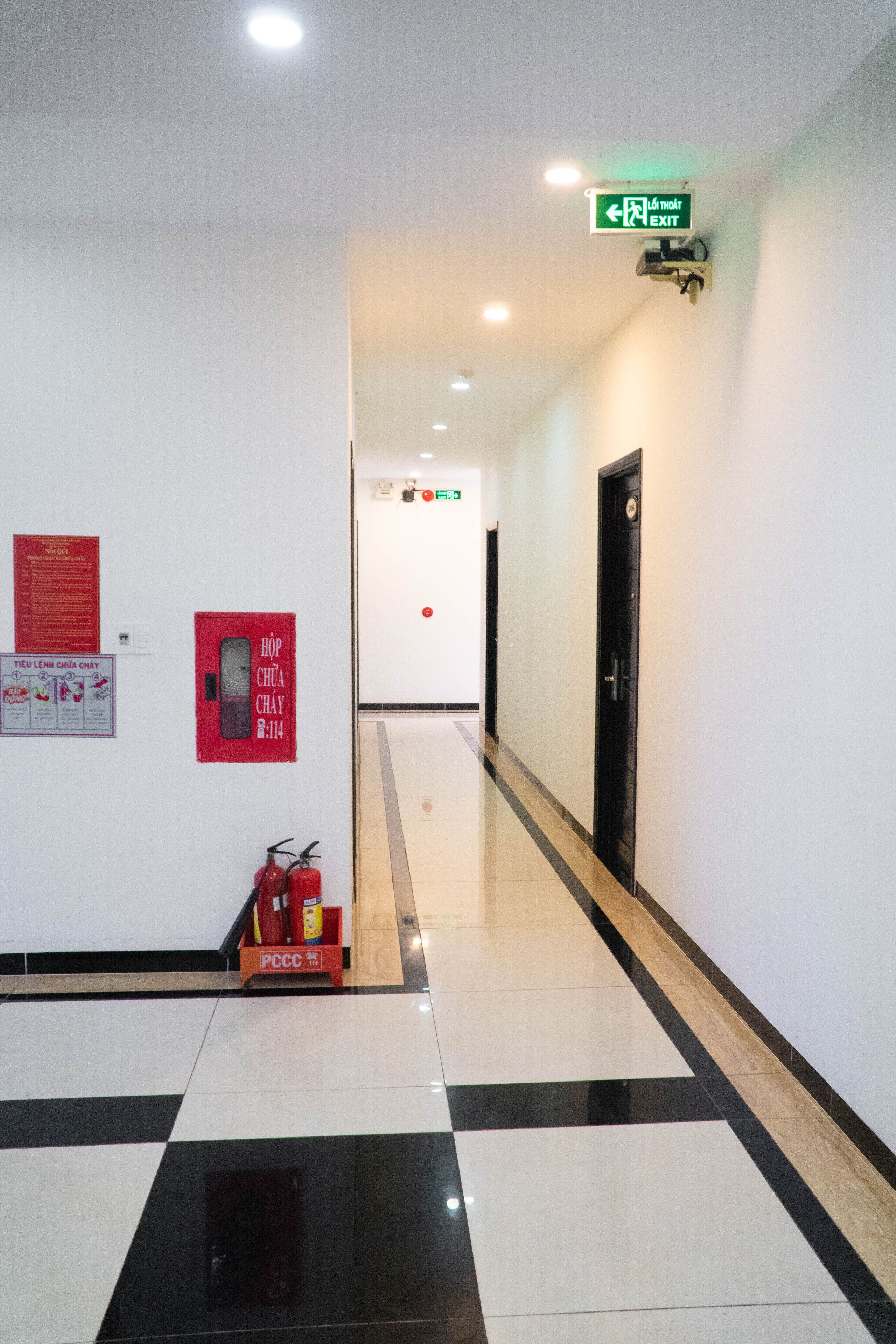 A clean, well-lit hallway with a black and white tiled floor, a fire extinguisher, and a fire safety sign on the wall.