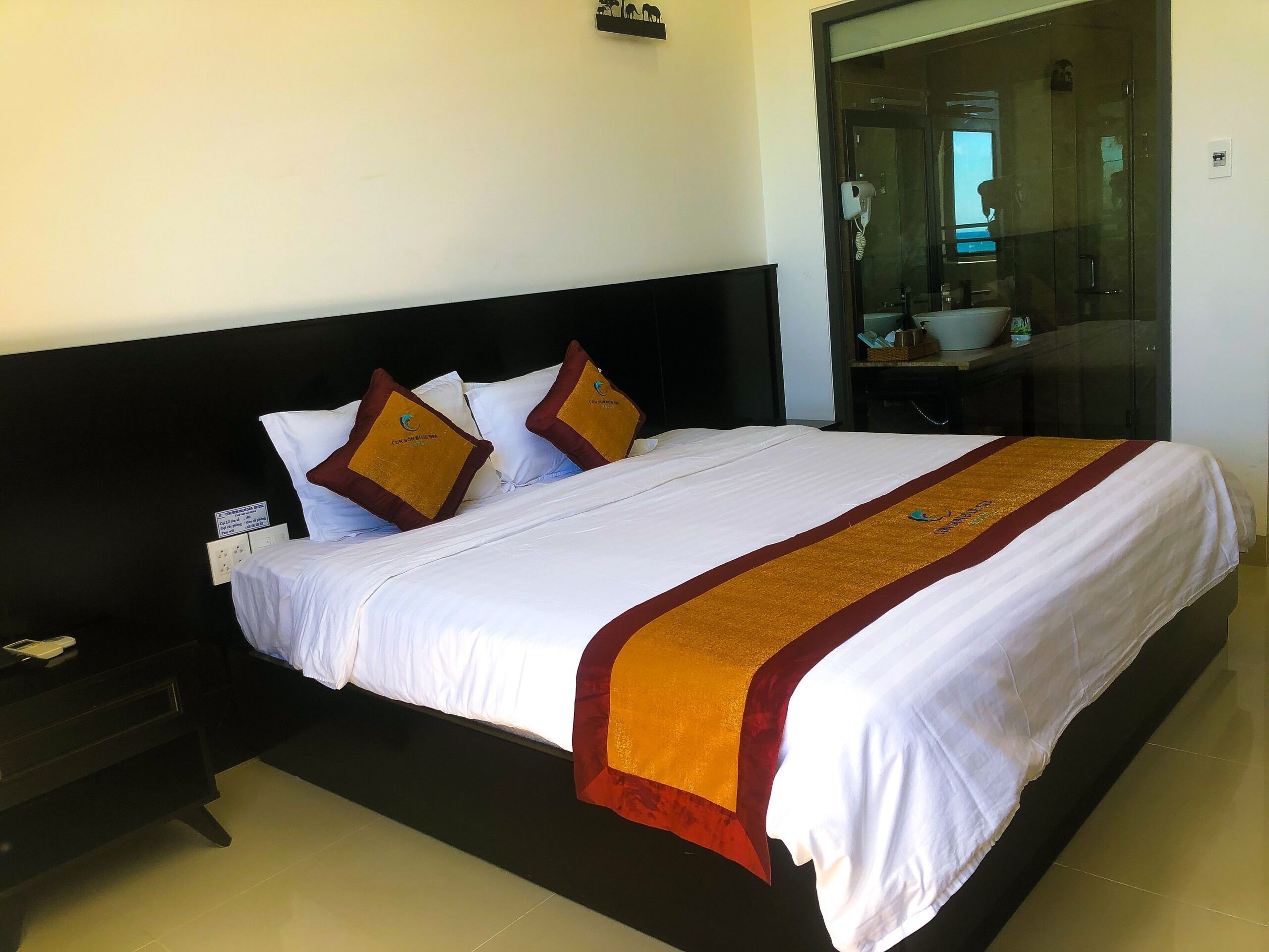 A hotel room with a large bed, a nightstand, a glass shower enclosure, and a small table with a mirror.