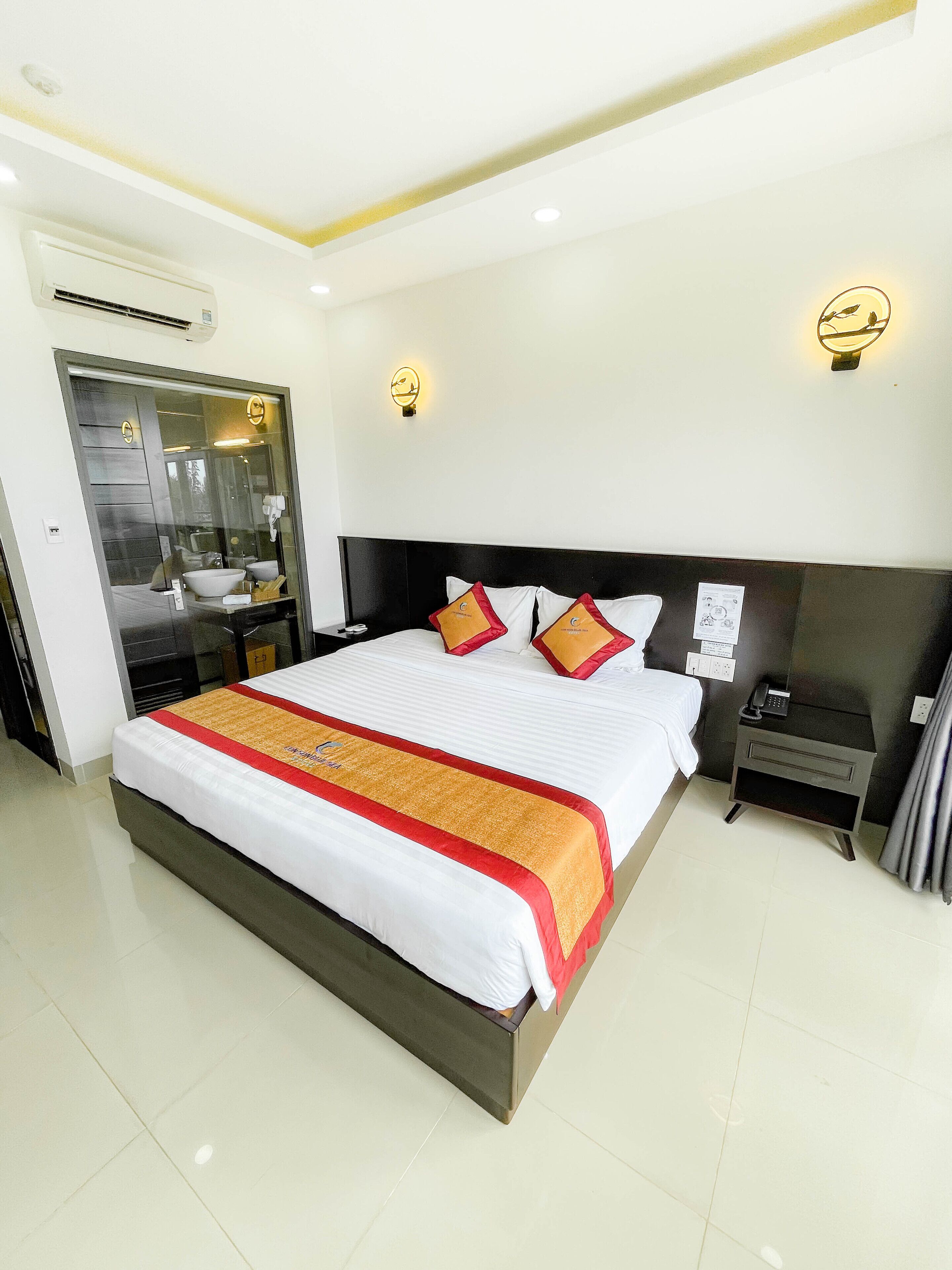 A modern hotel room with a large bed, a bedside table with a phone, and a mirror.