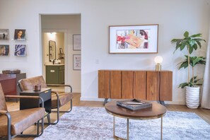 A modern living room with leather chairs, a round coffee table, a wooden cabinet, and a framed abstract painting. - Modern Wooded Retreat | Corporate Housing | Fenced Yard, Pets OK | Near Back 40 (Bella Vista)
