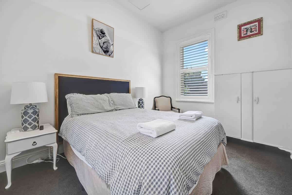 A bedroom with a bed, bedside table, lamp, and a window with blinds.