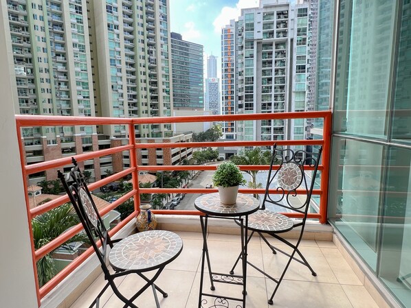 A balcony with a red railing, two chairs, a small table, and a potted plant.